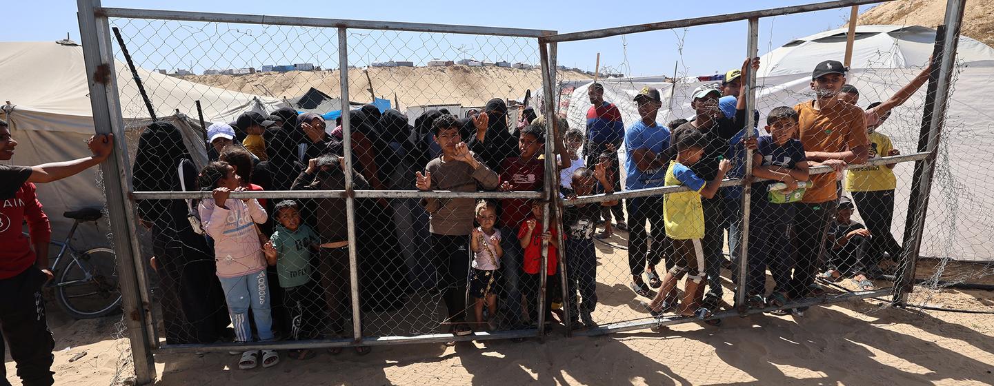 Un groupe d'enfants et d'adultes palestiniens se tient derrière une clôture en maillons dans un point de dépistage nutritionnel soutenu par l'UNICEF à Khan Yunis, dans le sud de la bande de Gaza.