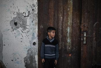 A young boy stands by a wall showing the signs of a missile attack.