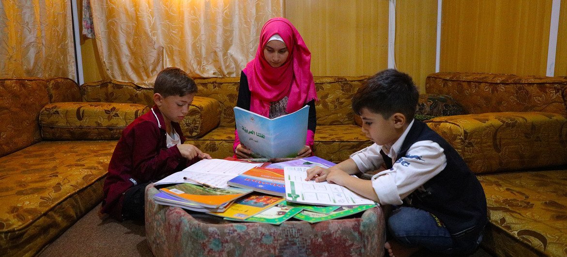 约旦难民营里的一名叙利亚少女在辅导她的弟弟和邻居的儿子学习。