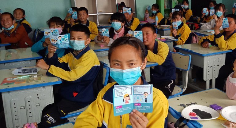 Alunos seguram folhetos com informações de saúde sobre Covid-19 em sala de aula na província de Qinghai, China.