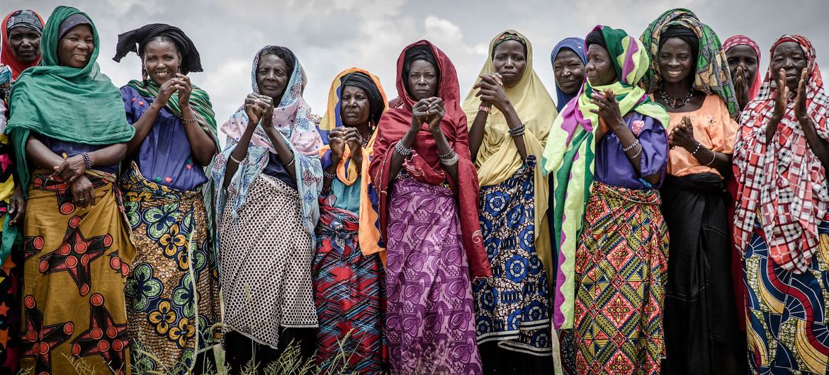 Un groupe de femmes vêtues de vêtements traditionnels colorés se tiennent dans un champ au Niger, applaudissant en attendant l'arrivée d'un convoi des Nations Unies .