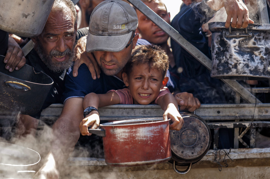 فلسطينيون في غزة بانتظار تلقي مساعدات غذائية في ظل انتشار الجوع وسوء التغذية، وشح الإمدادات التي يُسمح بدخولها إلى القطاع.