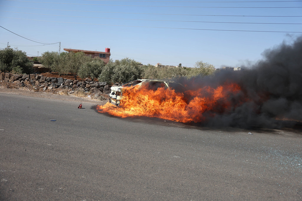 A vehicle burns as hostilities continue in Sweida, Syria.