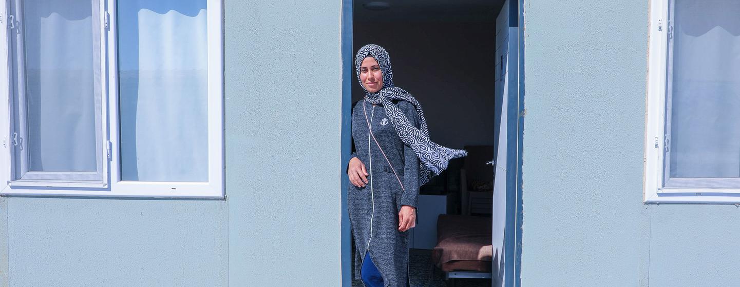Emel stands by the door of her new home – a 32-square-metre container she moved into with her husband and four children after living in a tent for three months.