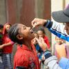 Mtoa chanjo wa kiume akimpa msichana mdogo chanjo ya polio nchini Madagaska kama sehemu ya kampeni ya afya ya jamii. Watoto wengine na wanajamii wanatazama nyuma.