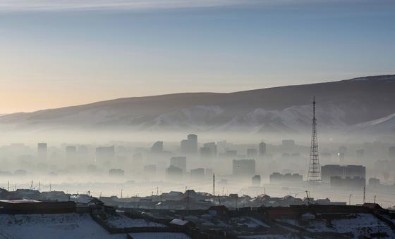 A hazy view of the Ulaanbaatar city skyline in Mongolia, with a snow-capped mountain range in the background.