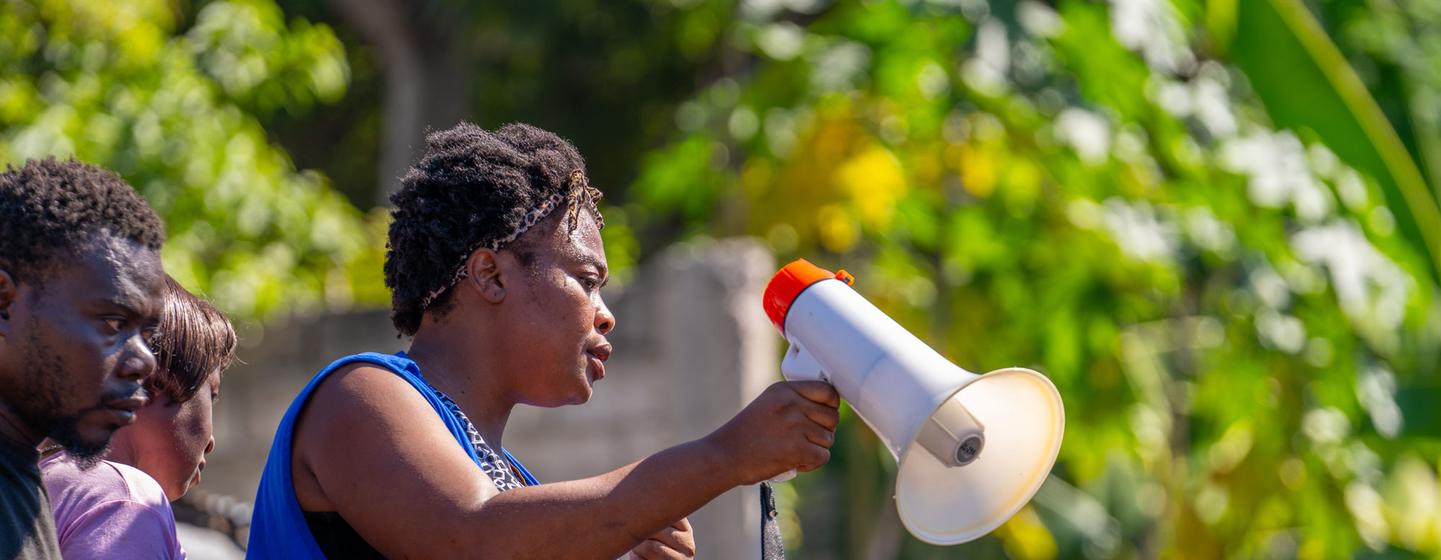 Un employé de l'OIM utilise un mégaphone pour guider les résidents lors d'une distribution d'aide sur un site de déplacés en Haïti.