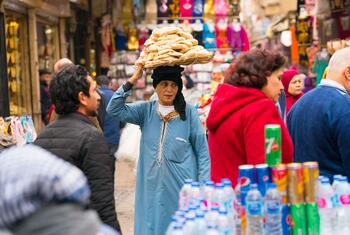 Une femme en robe bleue balance un gros panier de pain sur sa tête alors qu'elle se promène dans un marché animé au Caire, en Égypte.