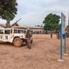 Un véhicule de maintien de la paix de l'ONU avec du personnel armé est stationné dans une zone poussiéreuse de la République centrafricaine, avec une foule de personnes locales rassemblées à l'arrière-plan.