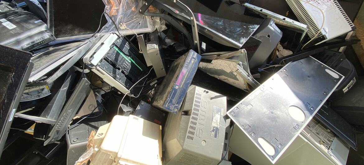 Uma pilha de dispositivos eletrónicos descartados, incluindo computadores, monitores e televisores, destacando a questão dos resíduos eletrónicos e a necessidade de eliminação e reciclagem adequadas.