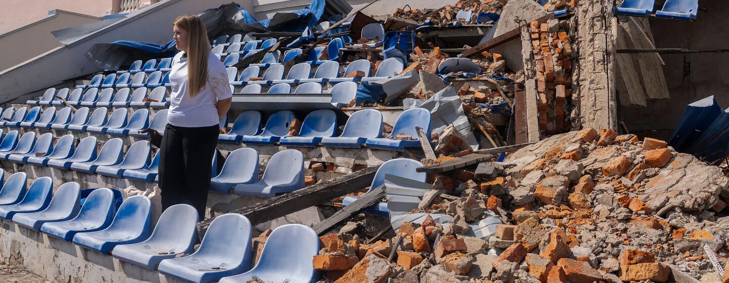 Une étudiante ukrainienne de 17 ans nommée Sofiia se tient parmi les sièges détruits d'un stade de Kharkiv, en Ukraine. La tribune a été endommagée par des bombardements, avec des décombres et des chaises en plastique brisées éparpillées. Sofiia, qui rêve de devenir médecin, fait partie d'un programme de récupération de l'apprentissage soutenu par l'UNICEF pour aider les élèves à rattraper l'éducation perturbée par la guerre.