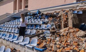 A 17-year-old Ukrainian student named Sofiia stands among the destroyed seats of a stadium in Kharkiv, Ukraine. The grandstand was damaged by shelling, with rubble and broken plastic chairs scattered around. Sofiia, who dreams of becoming a doctor, is part of a UNICEF-supported learning recovery program helping students catch up on education disrupted by the war.