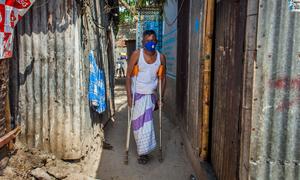 Un hombre con discapacidad camina usando muletas en un barrio de Bangladesh.