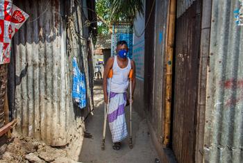 Un hombre con discapacidad camina usando muletas en un barrio de Bangladesh.
