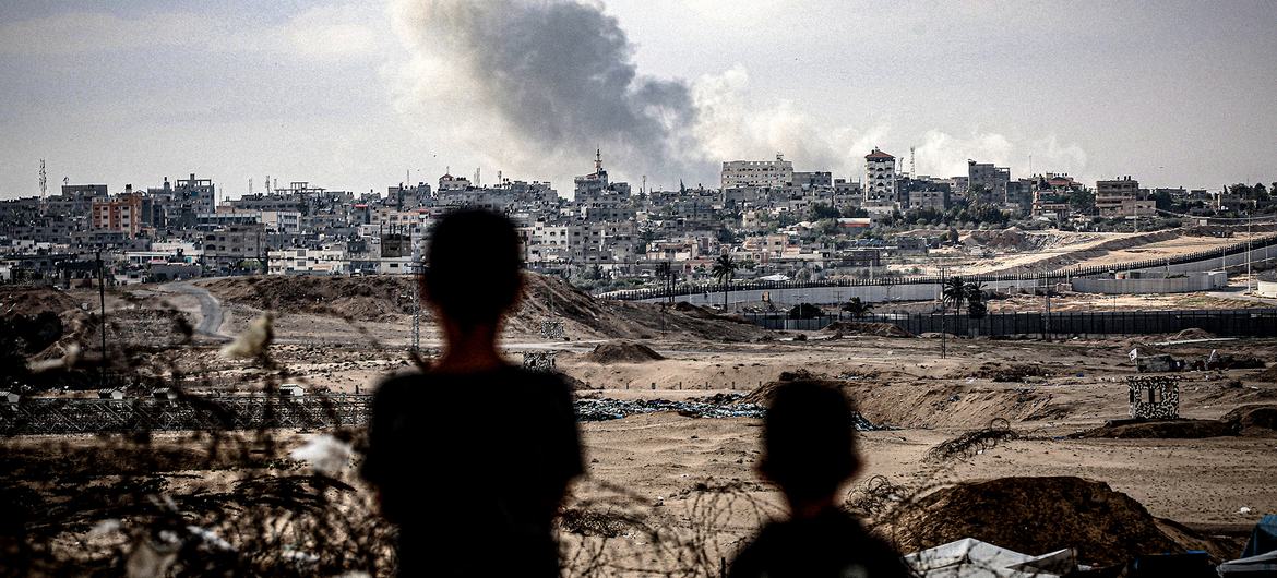 Duas crianças observam nuvens de fumaça subindo após ataque aéreo atingir a Cidade de Gaza