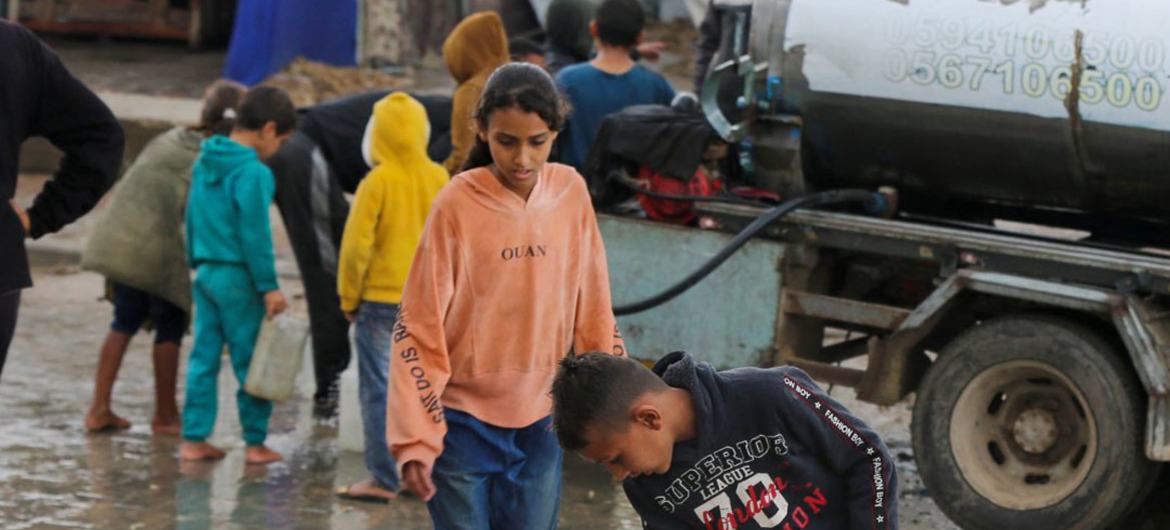 En Gaza, unos niños permanecen de pie en una calle inundada durante las lluvias invernales, recogiendo agua en un bidón amarillo.