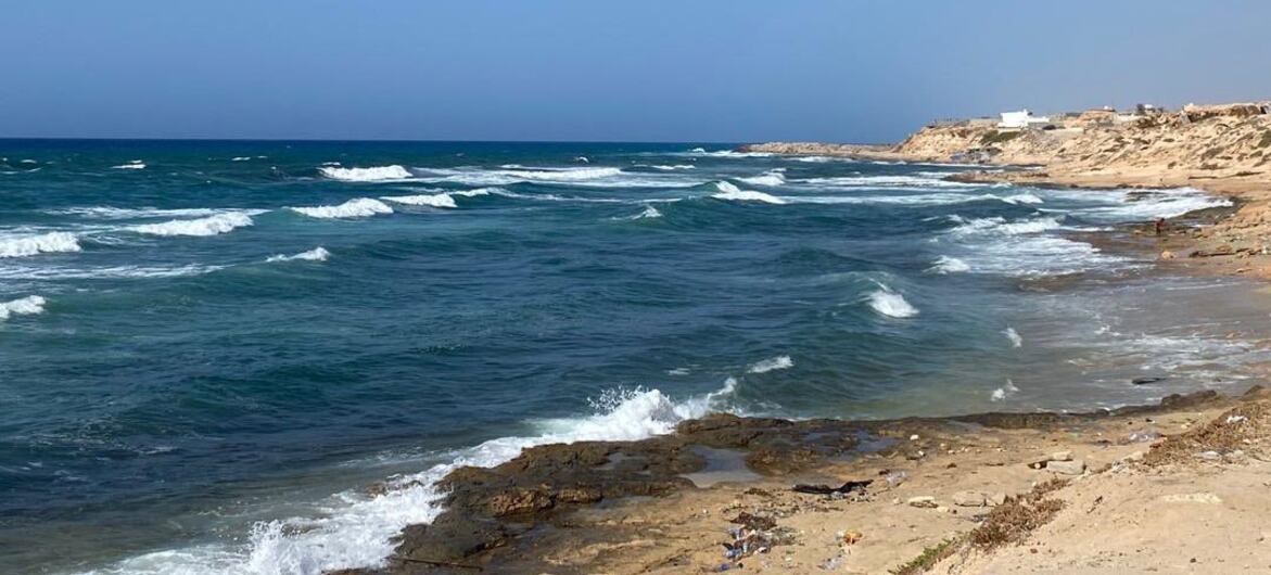 A coastal scene in Libya with waves crashing onto rocky shores, highlighting the ongoing humanitarian crisis where migrants are at risk of drowning in the Central Mediterranean.