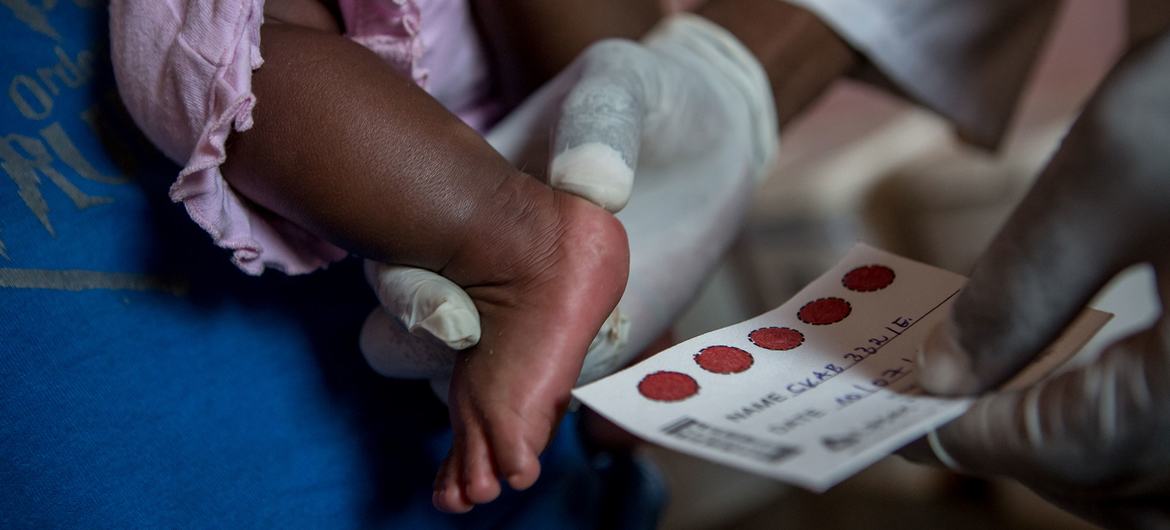 Le pied d'un bébé est tenu par un agent de santé portant des gants pour un prélèvement sanguin destiné à un test PCR de dépistage du VIH à la clinique de Kaboko, dans la ville de Kisenga, en RDC.