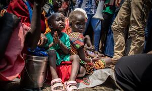 Children displaced by violence in Jonglei State, South Sudan, sit outside an episcopal church seeking humanitarian aid, with one child holding hands in prayer.