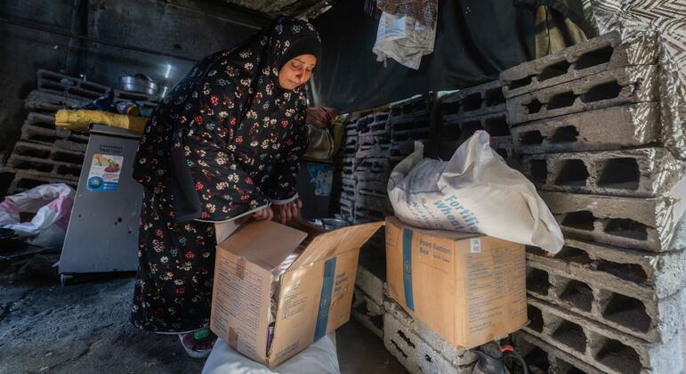 امرأة فلسطينية، أم عمر، تبحث عن زيت زهرة شمسية معزز داخل حزمة غذائية من برنامج الأغذية العالمي في خيمتها المؤقتة في مدينة غزة، محاطة بأحجار من منزلها المدمر.