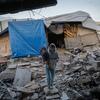 A woman, Sama, holds her 10-month-old child, Akram, as they stand amidst the rubble of their destroyed home in Al-Zarqaa, Gaza City. The family lives in a makeshift tent and relies on WFP assistance and hot meals from humanitarian organizations.