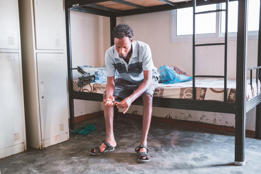 Jamal, un migrant éthiopien, est assis sur un lit superposé dans un refuge à Djibouti, en mettant ses chaussettes, à la recherche de son neveu enlevé au Yémen.