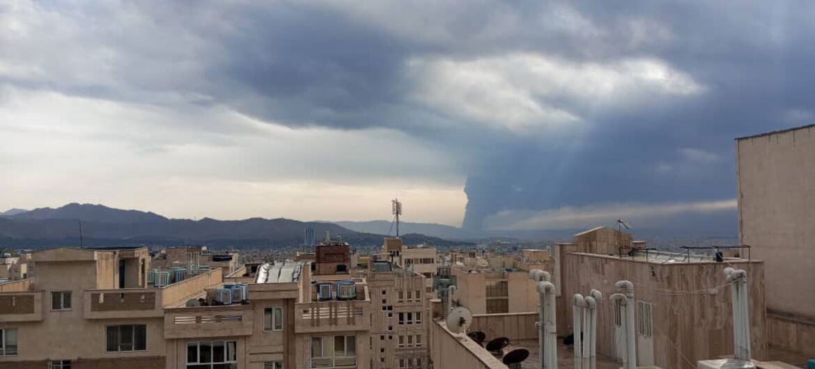 Una vista panorámica de los tejados de Teherán bajo una dramática nube de tormenta con lluvia en la distancia, con montañas visibles en el horizonte.