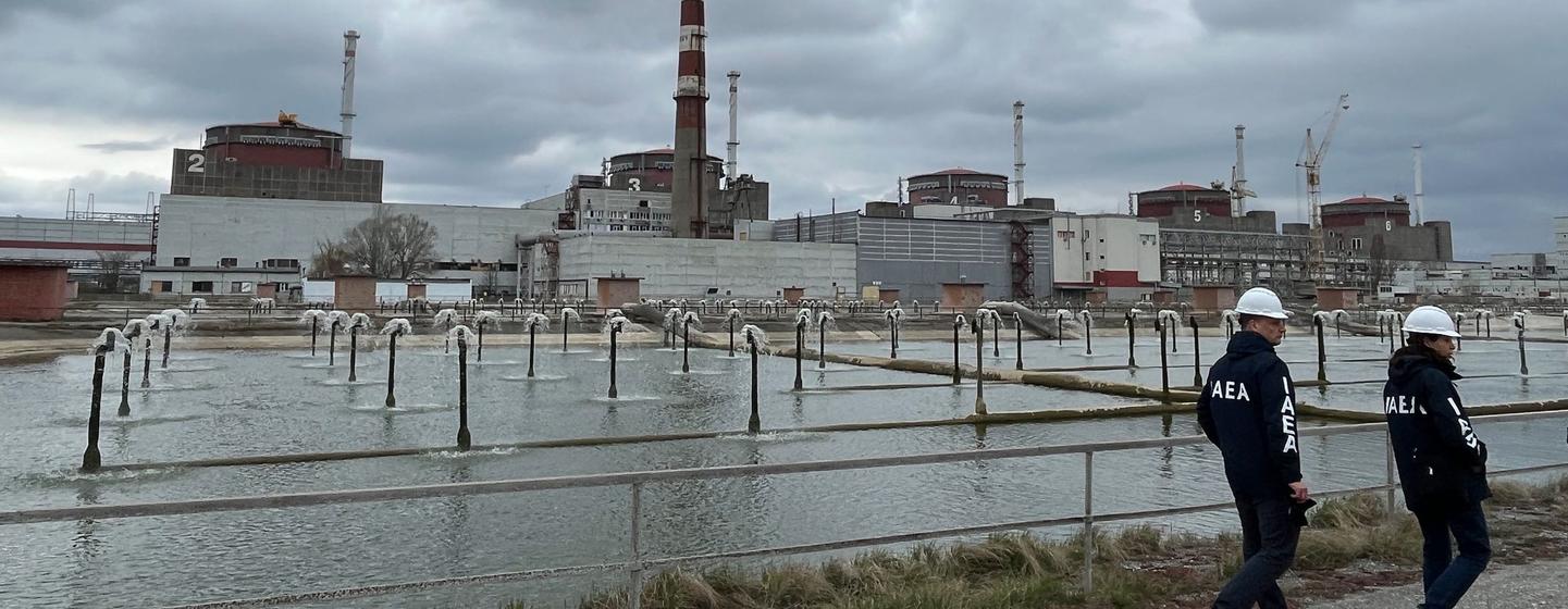Le directeur général de l'AIEA, Rafael Mariano Grossi, et un collègue passent devant un bassin de refroidissement avec en arrière-plan la centrale nucléaire de Zaporijjia.