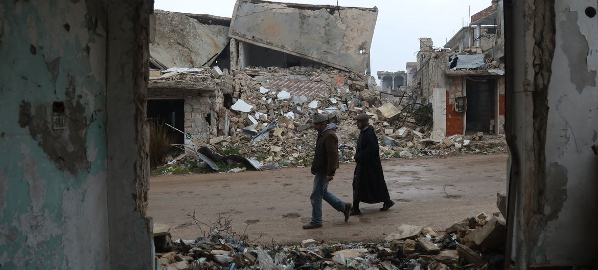 两个人走过被炸毁的叙利亚西部巴拉村的废墟。