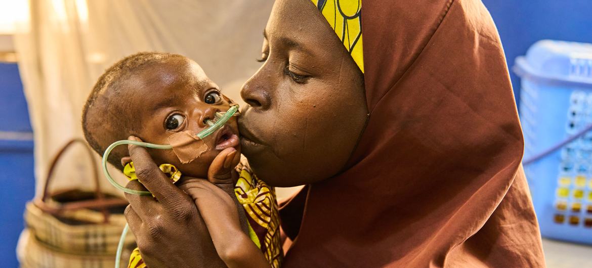 Au Nigéria, une femme embrasse un nourrisson malnutri sous oxygénothérapie dans un établissement de santé.