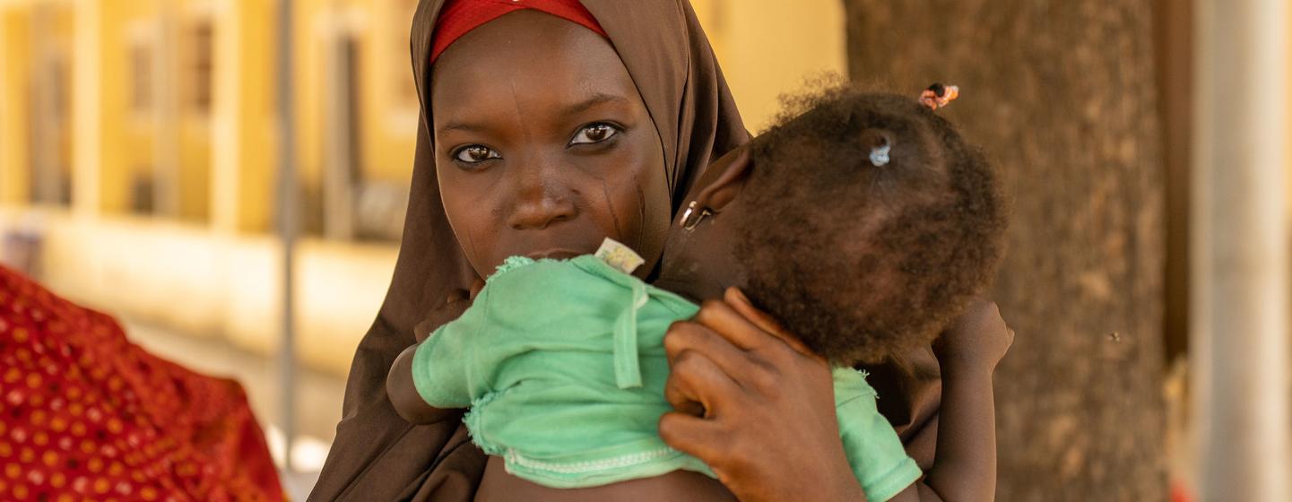 Une femme de Borno, au Nigéria, tient un jeune enfant dans ses bras.