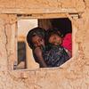 طفل وأمه ينظران من خلال نافذة في مجتمع السبعات بولاية كسلا.