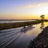 Um barco com várias pessoas a bordo navega por um canal nos pântanos costeiros de Samsuan, Pampanga, durante um pôr do sol dourado nas Filipinas.