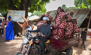 Pessoas, incluindo um homem em uma motocicleta e mulheres em trajes tradicionais, se reúnem para um evento público na região de Gabu, na Guiné-Bissau.