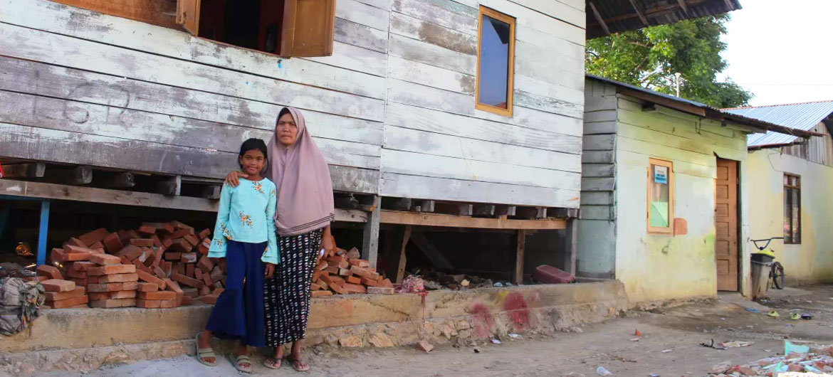 Une femme et une jeune fille se tiennent devant une maison traditionnelle en bois à Aceh, en Indonésie, dans le cadre d'un programme de financement islamique soutenu par l'UNICEF.