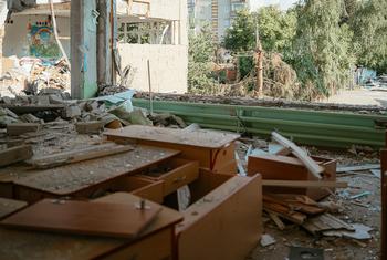 Intérieur en ruine d'une école maternelle endommagée à Tchouhouïv, en Ukraine, montrant des tables en bois renversées, des murs brisés et des décombres.