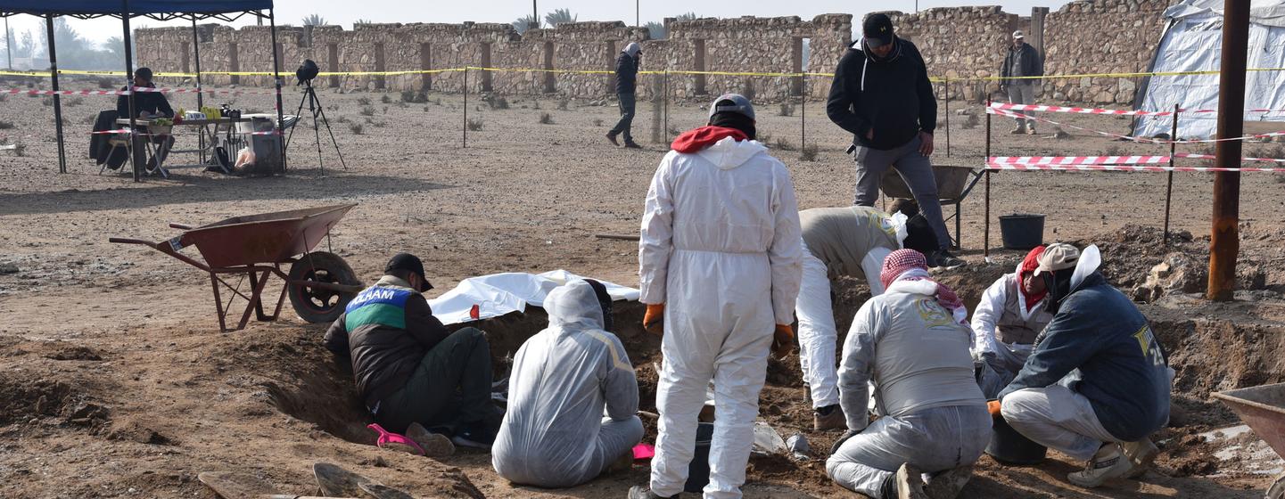 Des enquêteurs en combinaisons et uniformes de protection fouillent une fosse commune sur une scène de crime à Heet, dans la province d'Anbar, en Irak.