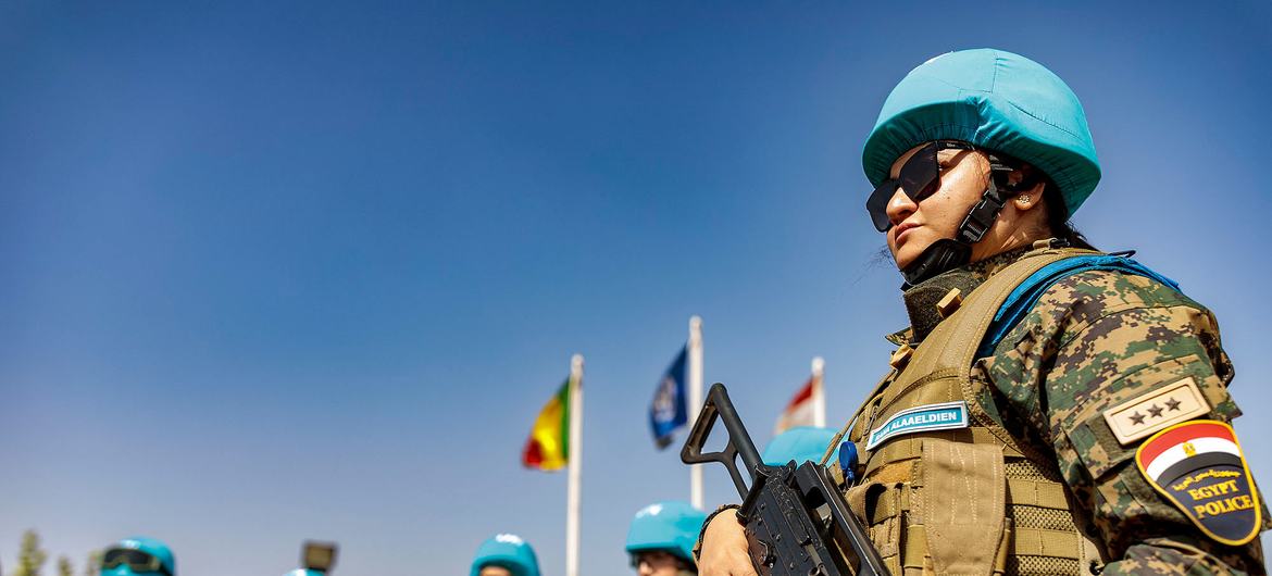 Policiais egípcios com capacetes azuis da ONU formam uma fileira com fuzis sob um céu azul claro.