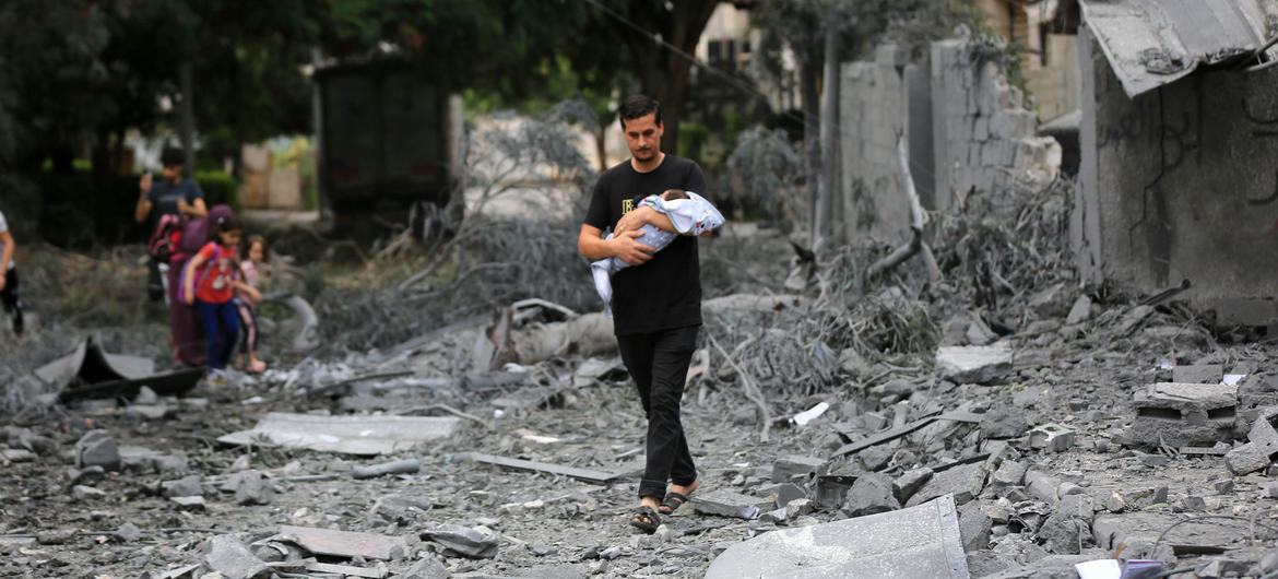 رجل يحمل رضيعا ويسير وسط الركام في حيه السكني المدمر في غزة.