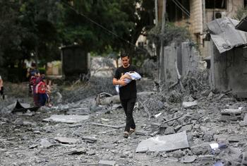 Un hombre que sostiene a un bebé camina entre los escombros de su vecindario destruido en Gaza.