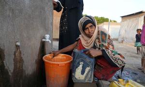 A woman collects water at a camp for people displaced by conflict in Yemen.