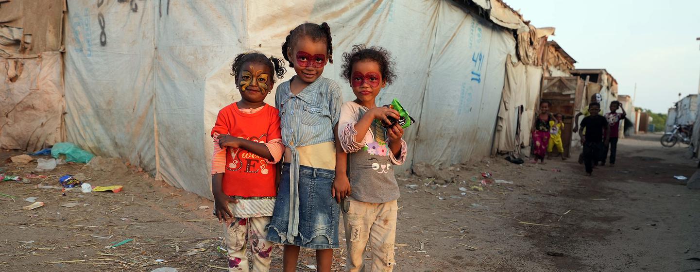 Trois jeunes filles se tiennent devant une tente temporaire dans un camp de déplacés au Yémen.