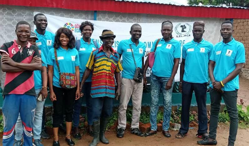 Un groupe d'individus, dont Nina Mireille Yankinon, se tient devant une banderole promouvant la paix et le développement en République centrafricaine, dans le cadre d'une initiative de consolidation de la paix menée par l'UNAOC et l'ILEL.
