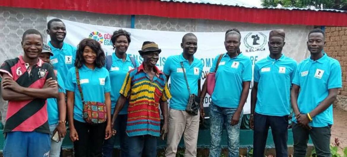 A group of individuals, including Nina Mireille Yankinon, stand together in front of a banner promoting peace and development in the Central African Republic. They are part of a peacebuilding initiative led by UNAOC and ILEL.