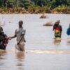 Pessoas atravessando águas de inundação em Moçambique, carregando pertences e ajudando-se mutuamente durante um desastre.