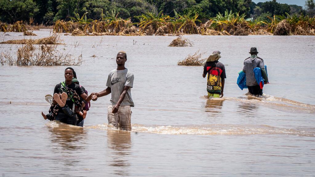 Personas atravesando las aguas de las inundaciones en Mozambique, llevando pertenencias y ayudándose mutuamente durante un desastre.