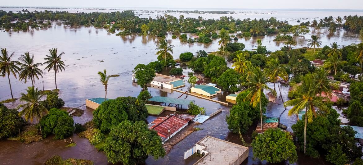 Uma imagem aérea de inundações severas em Moçambique, mostrando casas submergidas e palmeiras cercadas por águas de inundação marrom.