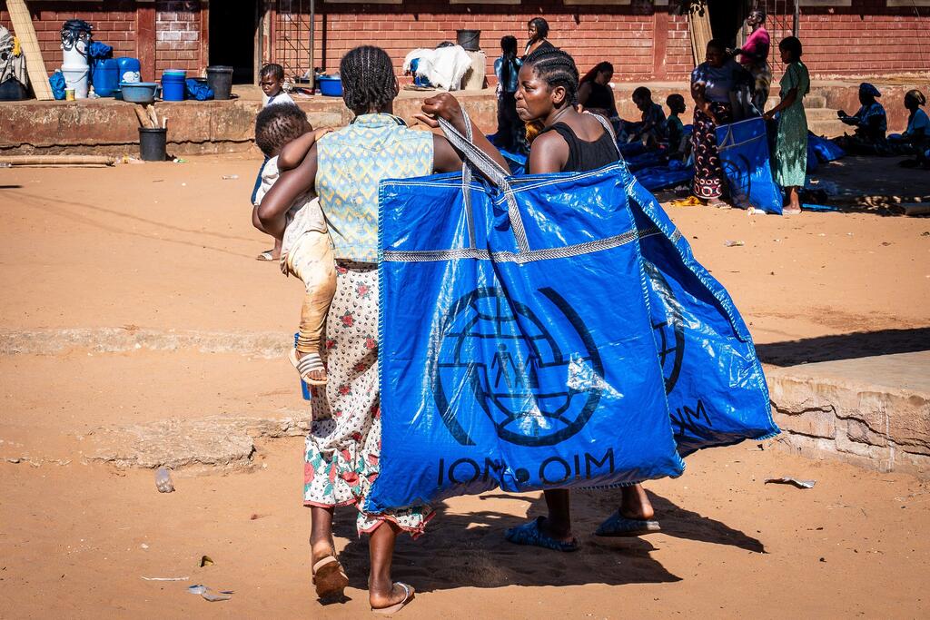 Mwanamke akiwa amebeba mtoto na begi kubwa ya rangi ya bluu ya misaada ya IOM huku akitembea katika eneo lililoathiriwa na mafuriko nchini Msumbiji.