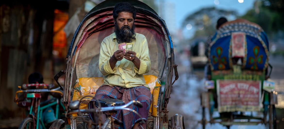Un tireur de rickshaw au Bangladesh est assis dans son rickshaw et compte ses gains, qui semblent être des billets Taka du Bangladesh.
