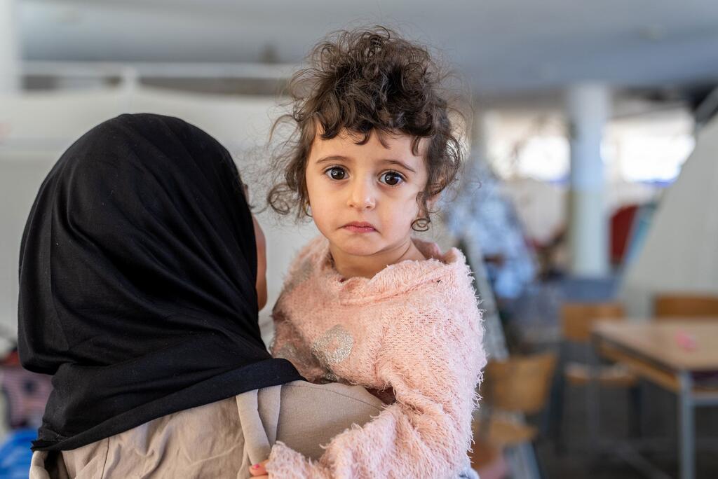 Fatima, une petite fille de 2 ans, avec des cheveux bouclés et un pull rose, regarde la caméra alors qu'elle est tenue par sa sœur Fadak, 12 ans, à l'école Omar Faroukh à Beyrouth, au Liban, qui sert d'abri pour les familles déplacées.